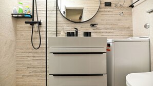 A bathroom with a modern design, featuring a white sink, a mirror, and a shower area. - New, close to the beach apartment with parking (Mastrinka)