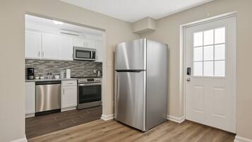 A modern kitchen with stainless steel appliances, white cabinetry, and a wooden floor.
