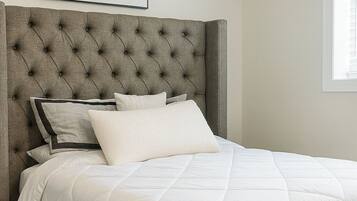 A bedroom with a tufted headboard, a quilted bedspread, and a framed abstract artwork on the wall.