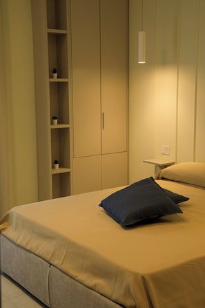 A bedroom with a bed, a nightstand, a shelf with potted plants, and a wardrobe. - Domus Vivian (Bellizzi)