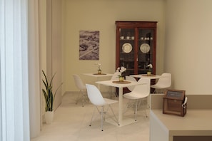 A dining area with white chairs, a wooden cabinet with glass doors, and a table with a plant. - Domus Vivian (Bellizzi)