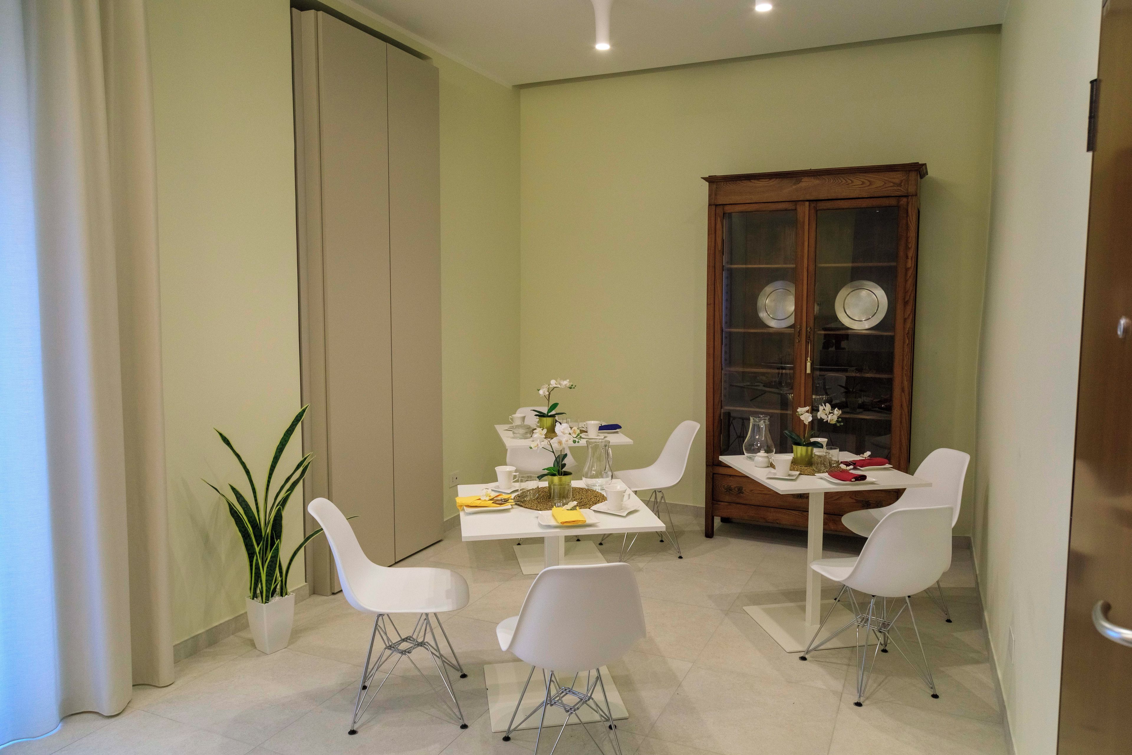 A dining area with a white table, four white chairs, a wooden cabinet with glass doors, and a potted plant.