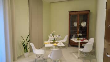 A dining area with a white table, four white chairs, a wooden cabinet with glass doors, and a potted plant.