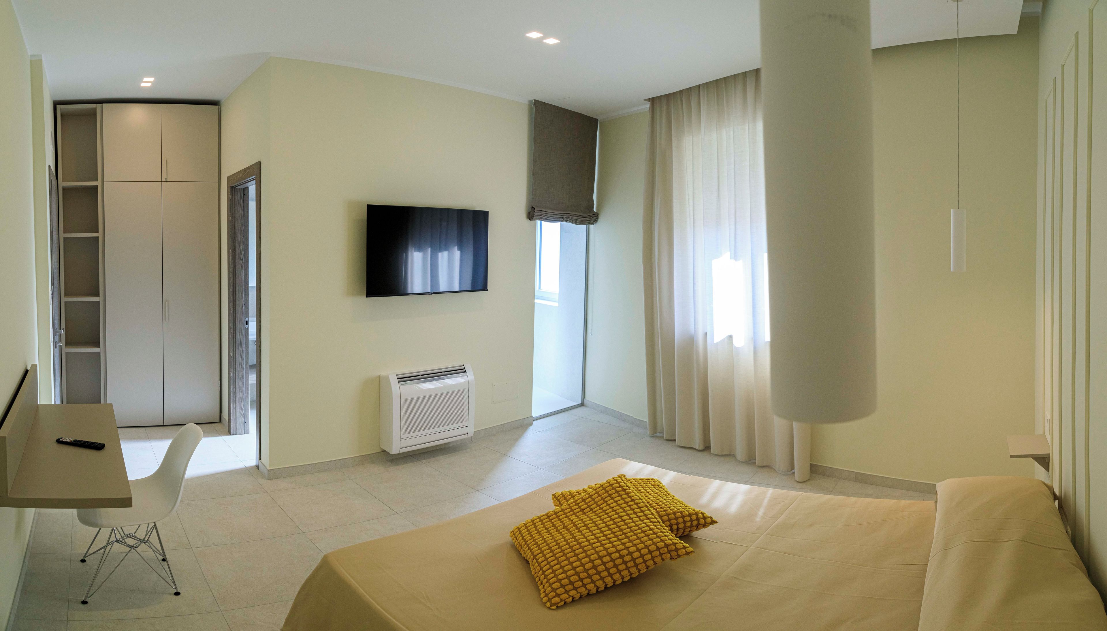 A hotel room with a bed, a desk, a chair, a TV, a window with curtains, and a wardrobe.