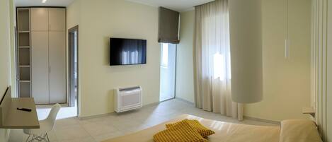 A hotel room with a bed, a desk, a chair, a TV, a window with curtains, and a wardrobe.