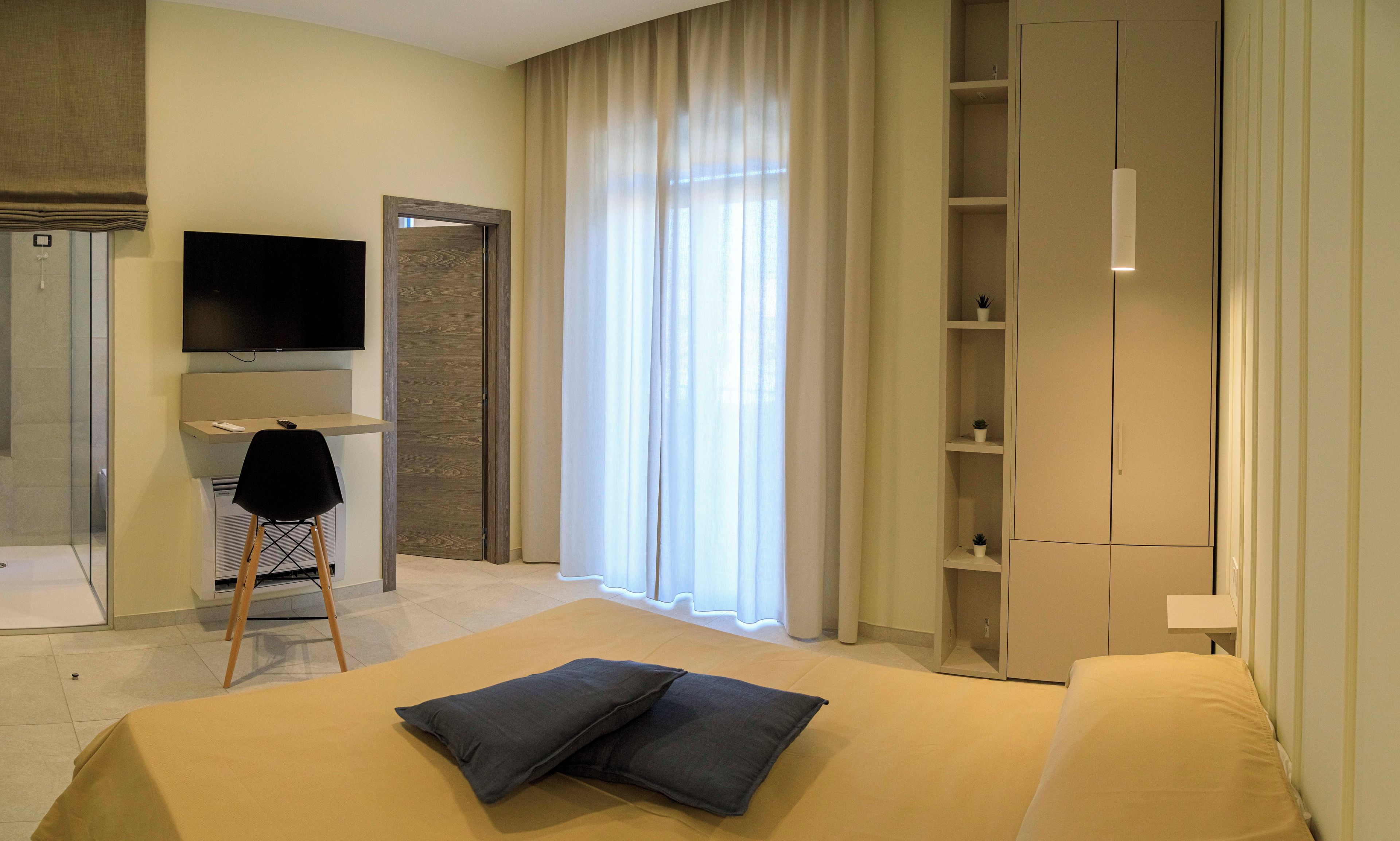 A modern hotel room with a bed, a desk, a TV, and a wardrobe.