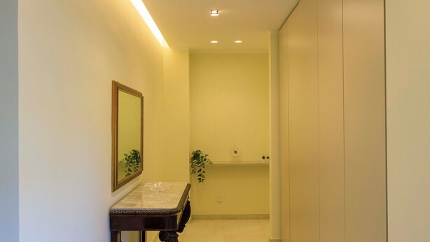 Un couloir avec une table surmontée d’un plateau en marbre, un miroir et une plante.