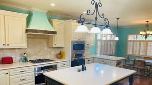 Une cuisine moderne avec des meubles blancs, un îlot central doté de tabourets de bar, des appareils en acier inoxydable et un mur d’accent de couleur turquoise.