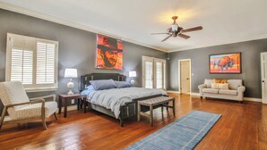 Une chambre à coucher comprenant un lit, une chaise, un canapé, un ventilateur de plafond et des œuvres d’art accrochées aux murs.