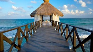 A wooden pier leading to a thatched-roof structure with white curtains, overlooking the ocean. - 2BD Grand Bliss Vidanta Resort RM (Playa del Carmen)
