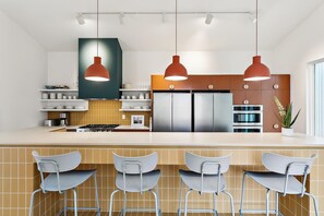 Een moderne keuken met een centraal eiland, hangende lampen en een potplant.