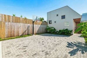 Un patio trasero empedrado con un aro de baloncesto, una valla de madera y un edificio moderno con ventanas.