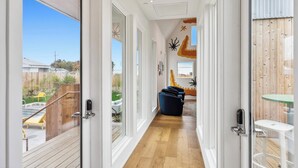 Un pasillo con piso de madera, una puerta de cristal que da a un balcón y una pequeña mesa con un taburete.
