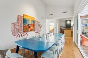 Un comedor moderno con una mesa azul y sillas blancas, un cuadro colorido en la pared y una cocina al fondo.