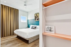 Een slaapkamer met een bed, gordijnen, een plafondventilator, een wandlamp en een plank met kunstwerken.