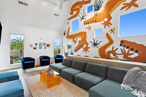 A modern living room with a grey sofa, blue armchairs, and a large wall mural of stylized sea creatures.