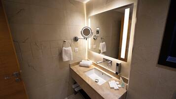 A modern bathroom with a marble-tiled wall, a large mirror with integrated lighting, a sink with a vanity, and a towel rack.