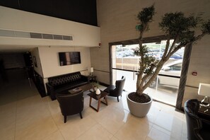 A modern lobby with a sofa, chairs, a coffee table, a TV, and a large potted tree. - Gloria Boutique Hotel (Amman)