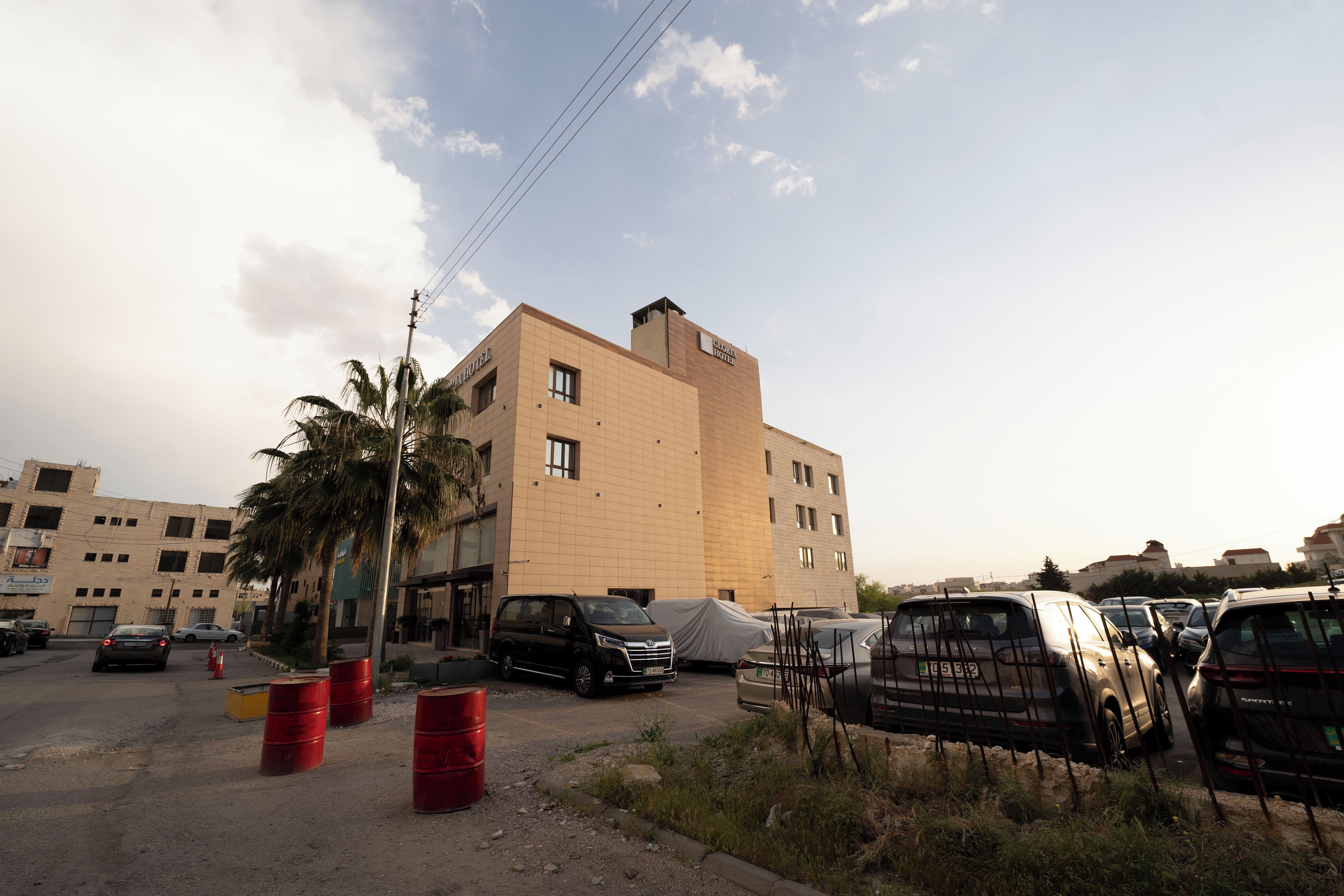 A multi-story building with a beige facade, parked cars, and palm trees.