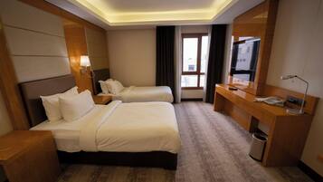 Une chambre d’hôtel avec deux lits, un bureau, une télévision et une fenêtre avec des rideaux.