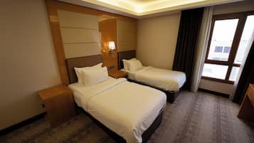 Habitación de hotel con dos camas, una mesita de noche, una lámpara y un ventanal con cortinas.