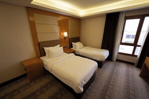 A hotel room with two beds, a nightstand, a lamp, and a large window with curtains. - Gloria Boutique Hotel (Amman)