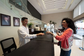 A reception area with a glass staircase, framed portraits on the wall, and a reception desk. - Gloria Boutique Hotel (Amman)