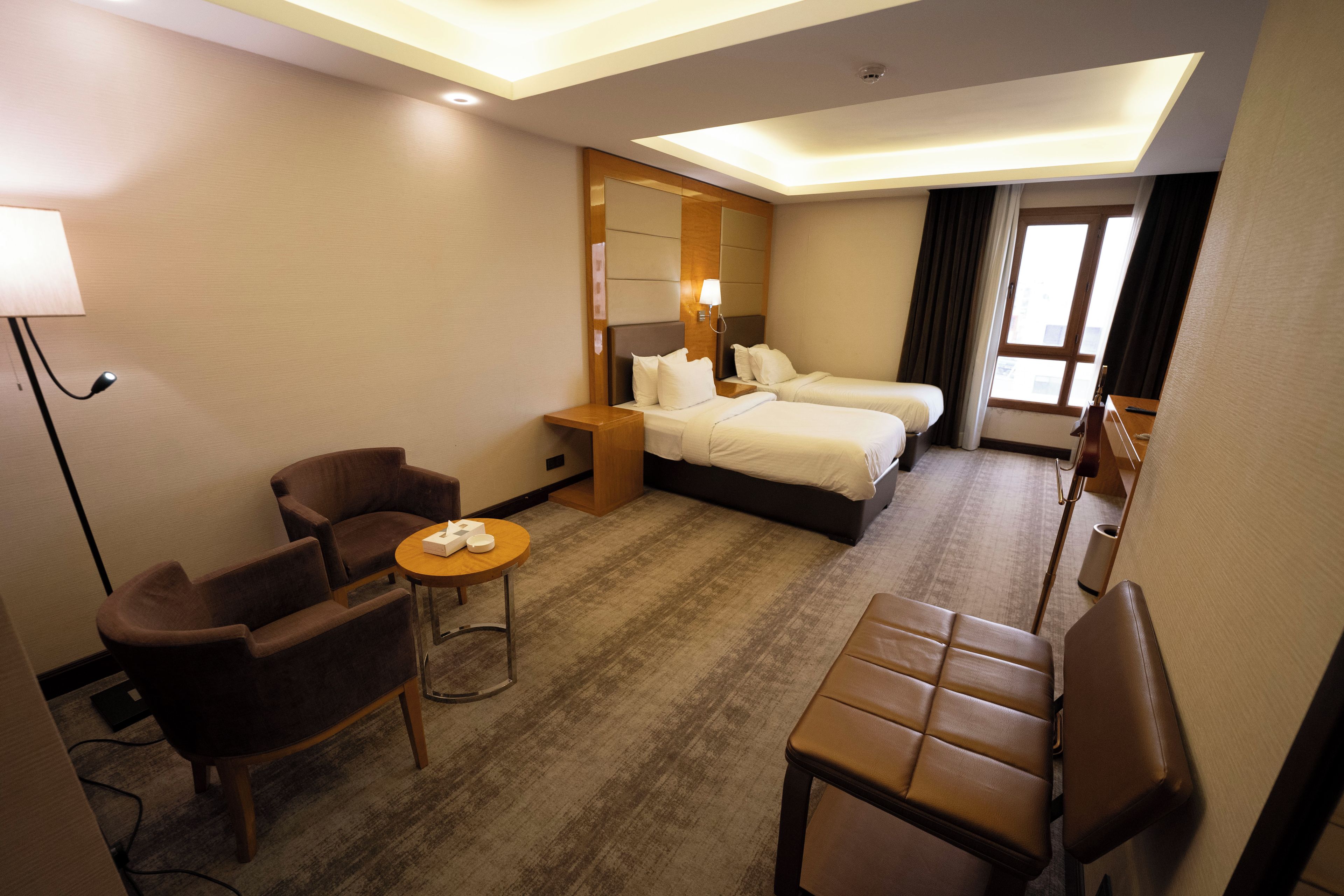 A hotel room with two beds, a desk, a chair, and a small table.