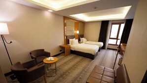 A hotel room with two beds, a desk, a chair, and a small table. - Gloria Boutique Hotel (Amman)