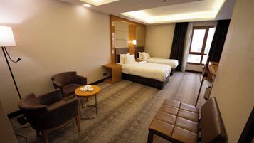A hotel room with two beds, a desk, a chair, and a small table.