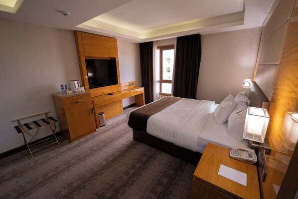 A hotel room with a bed, bedside table, TV, wooden desk, and a window with curtains. - Gloria Boutique Hotel (Amman)