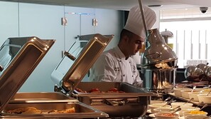 A buffet setup with various food containers and a chef in uniform. - Gloria Boutique Hotel (Amman)