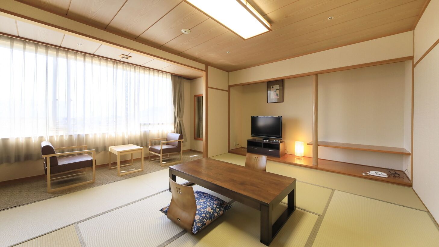 Ett traditionellt japanskt rum med tatamimattor på golvet, ett lågt bord, en soffa, en tv och en skjutdörr.