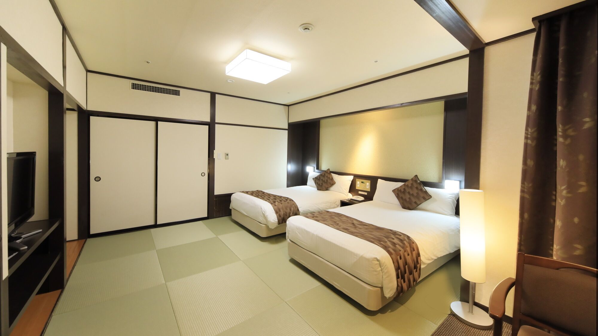 Habitación de hotel con dos camas, televisión, escritorio y un espejo grande.