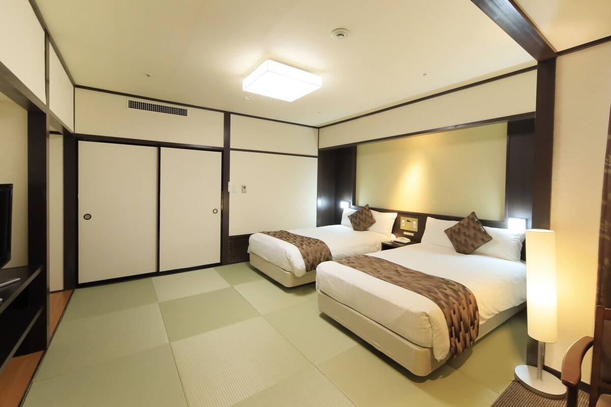 Habitación de hotel con dos camas, televisión, escritorio y un espejo grande.