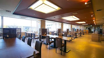 A spacious indoor area with multiple tables and chairs, large windows allowing natural light, and a modern ceiling design.