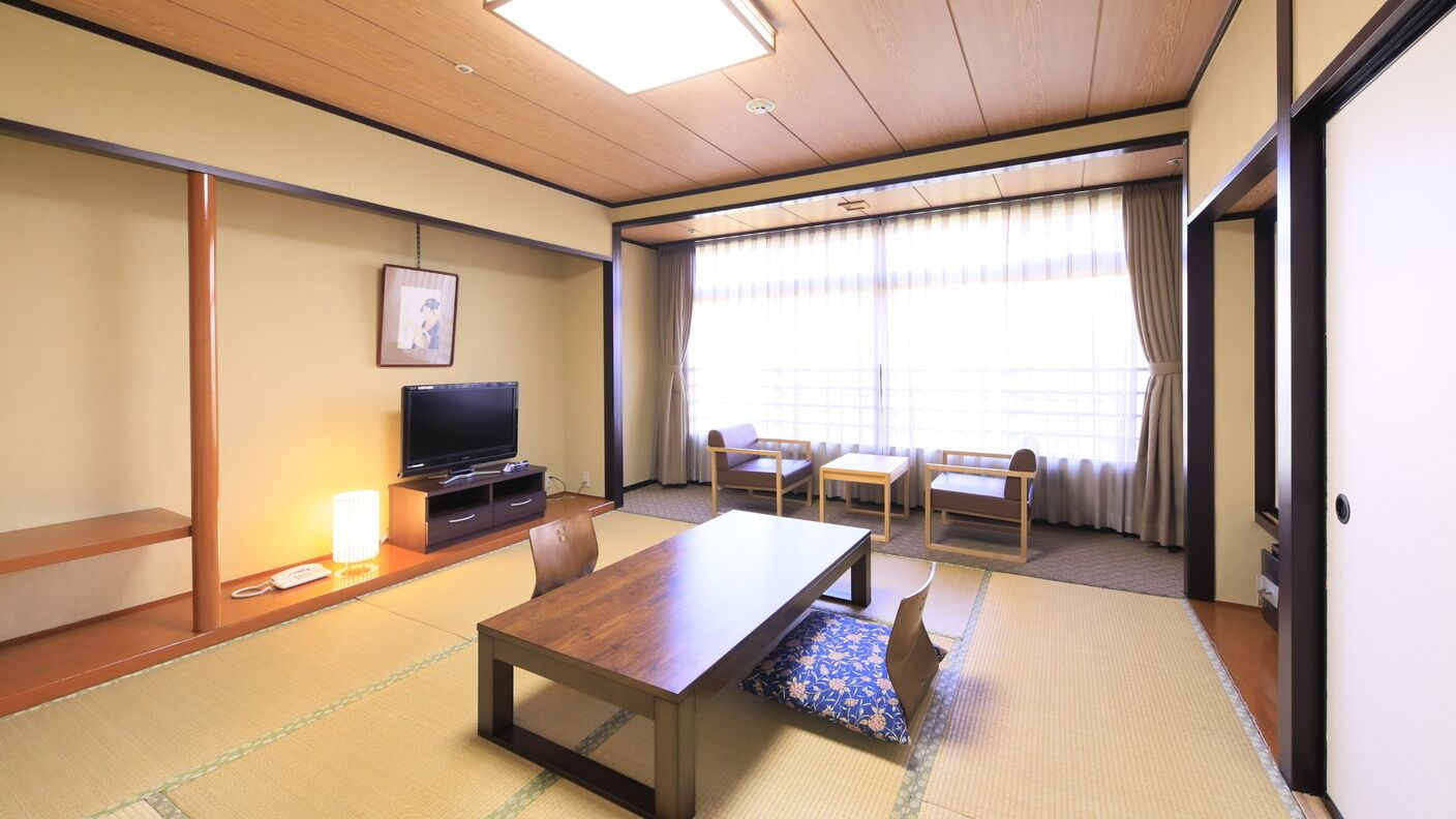 Ett traditionellt japanskt rum med tatamimattor på golvet, en tv, ett träbord och en soffa.