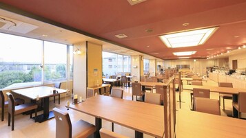 Uma ampla sala de jantar com várias mesas e cadeiras, grandes janelas com vista para o exterior e um design de teto moderno com iluminação embutida.