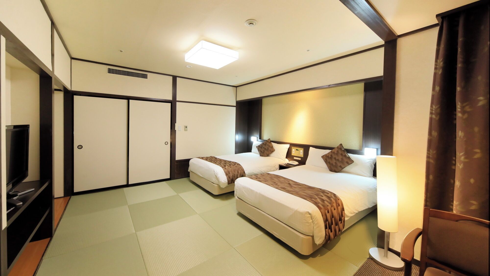 Una habitación de hotel con dos camas, televisor, escritorio y un espejo grande.