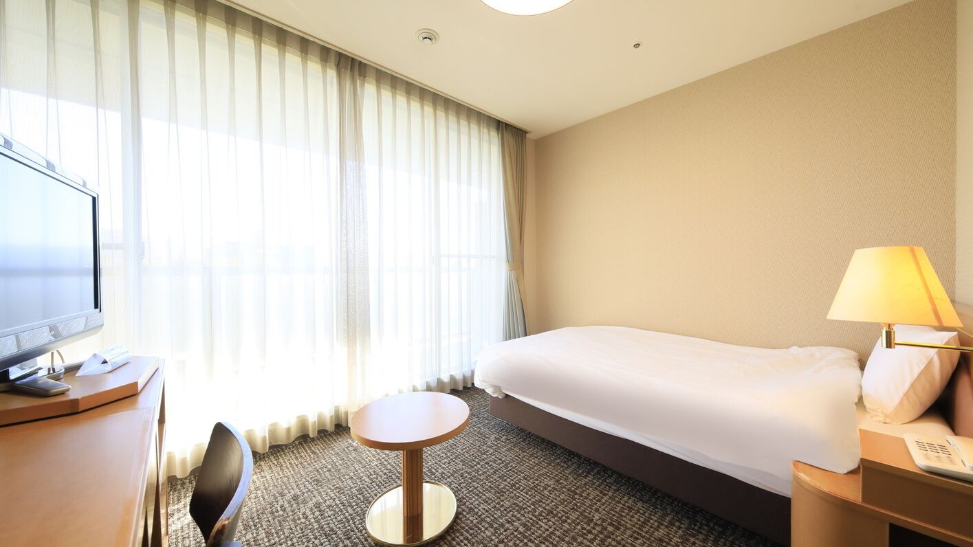 Habitación de hotel con cama, escritorio, computadora, silla, lámpara y ventana con cortinas.