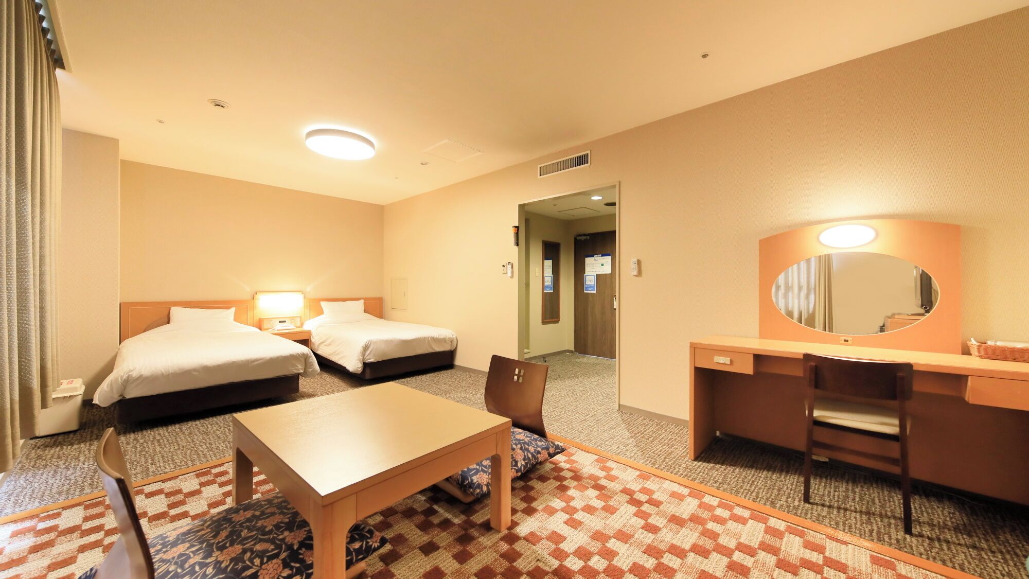 Habitación de hotel con dos camas, un escritorio, una silla, una mesa, un espejo y suelo alfombrado.