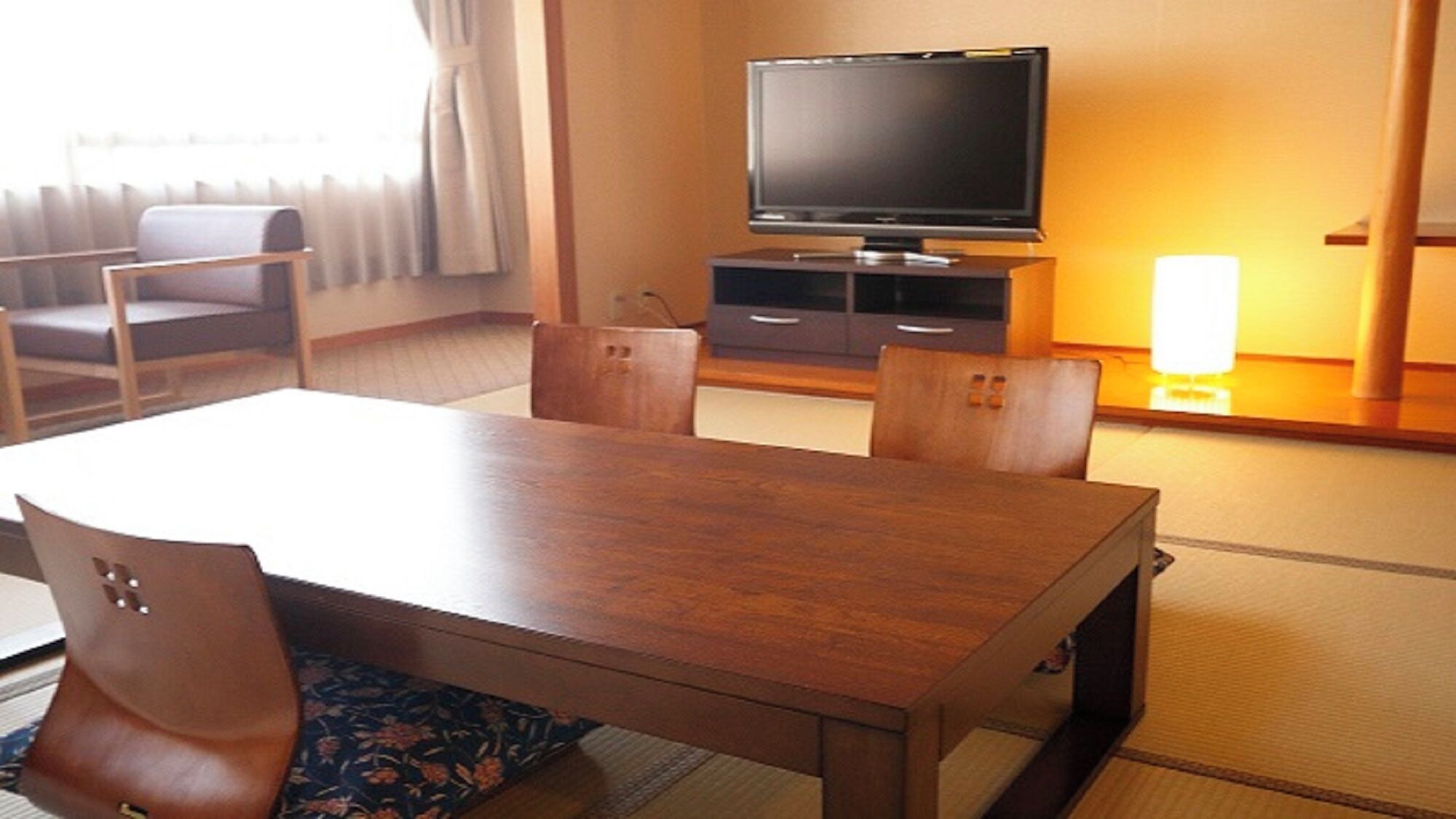 Ett hotellrum med ett matbord och stolar i trä, en tv på ett stativ och en lampa.