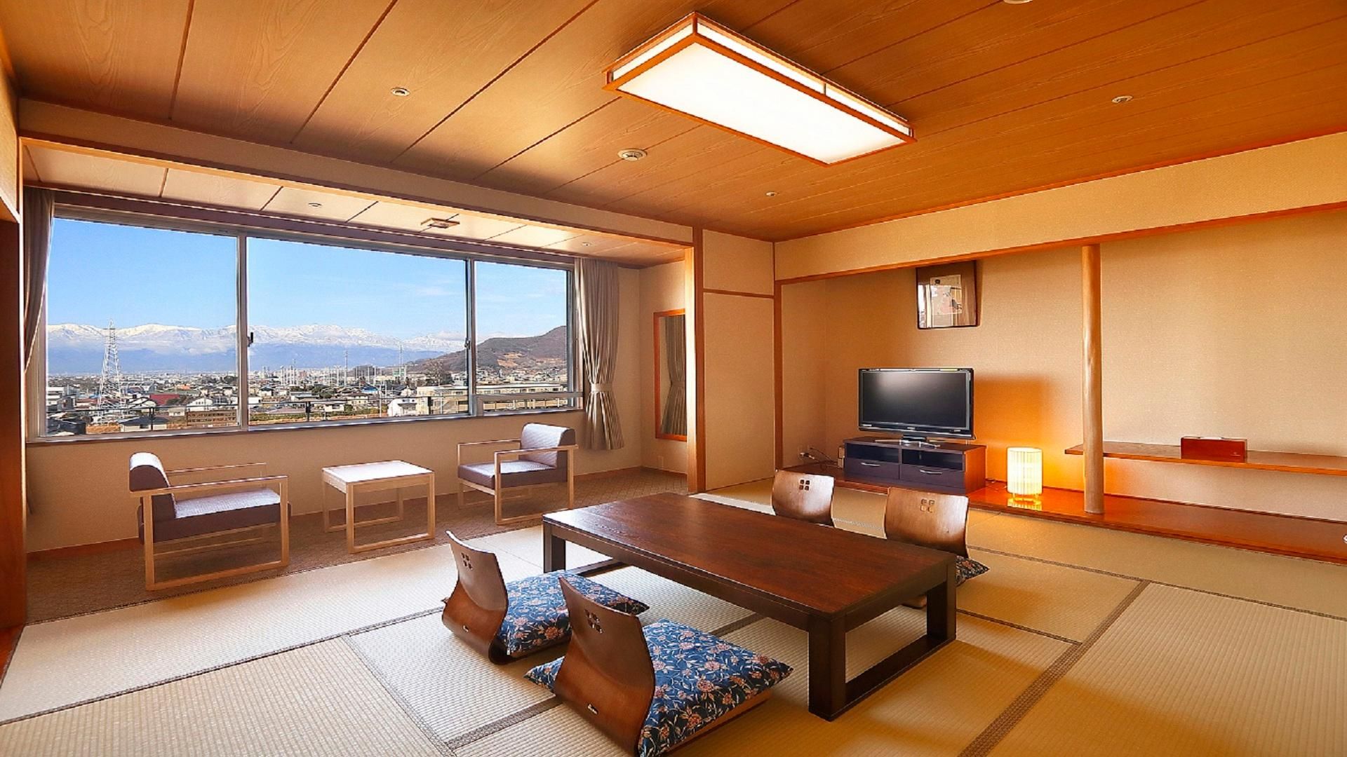 A hotel room with a large window, a dining table, chairs, a TV, and a small shelf.