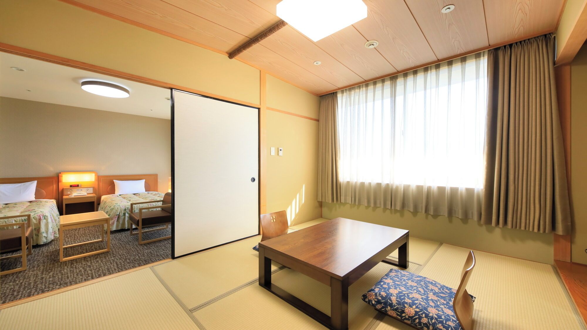 Habitación de hotel tradicional al estilo japonés, con suelo de tatami, una mesa de madera, un sofá y un puertas correderas.