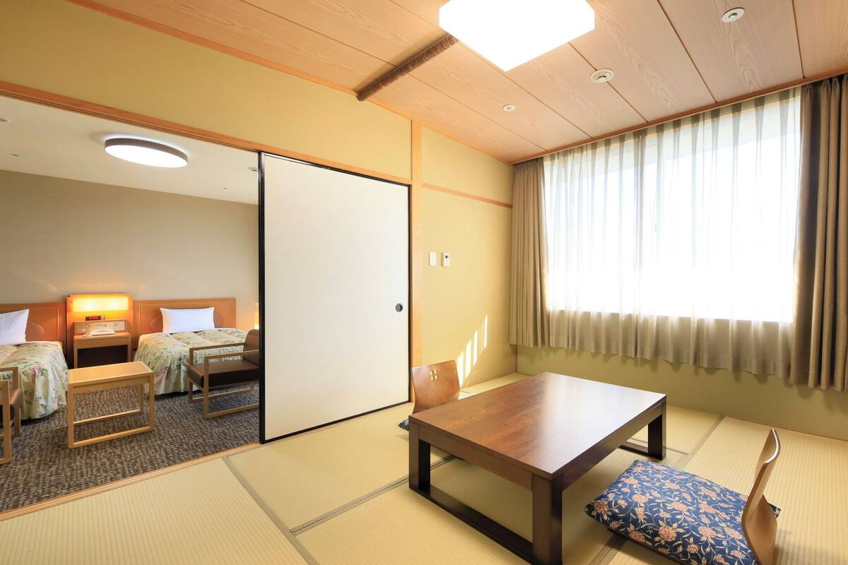 Habitación de hotel tradicional al estilo japonés, con suelo de tatami, una mesa de madera, un sofá y un puertas correderas.
