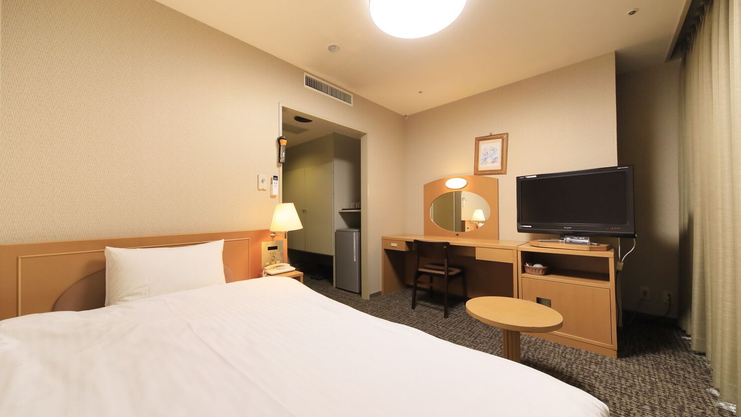 Ett hotellrum med en säng, ett skrivbord, en tv och ett litet bord.