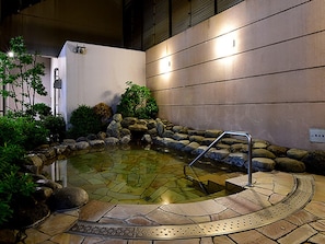 Uma área de águas termais com piscina de pedra, degraus e guarda-corpo de metal.