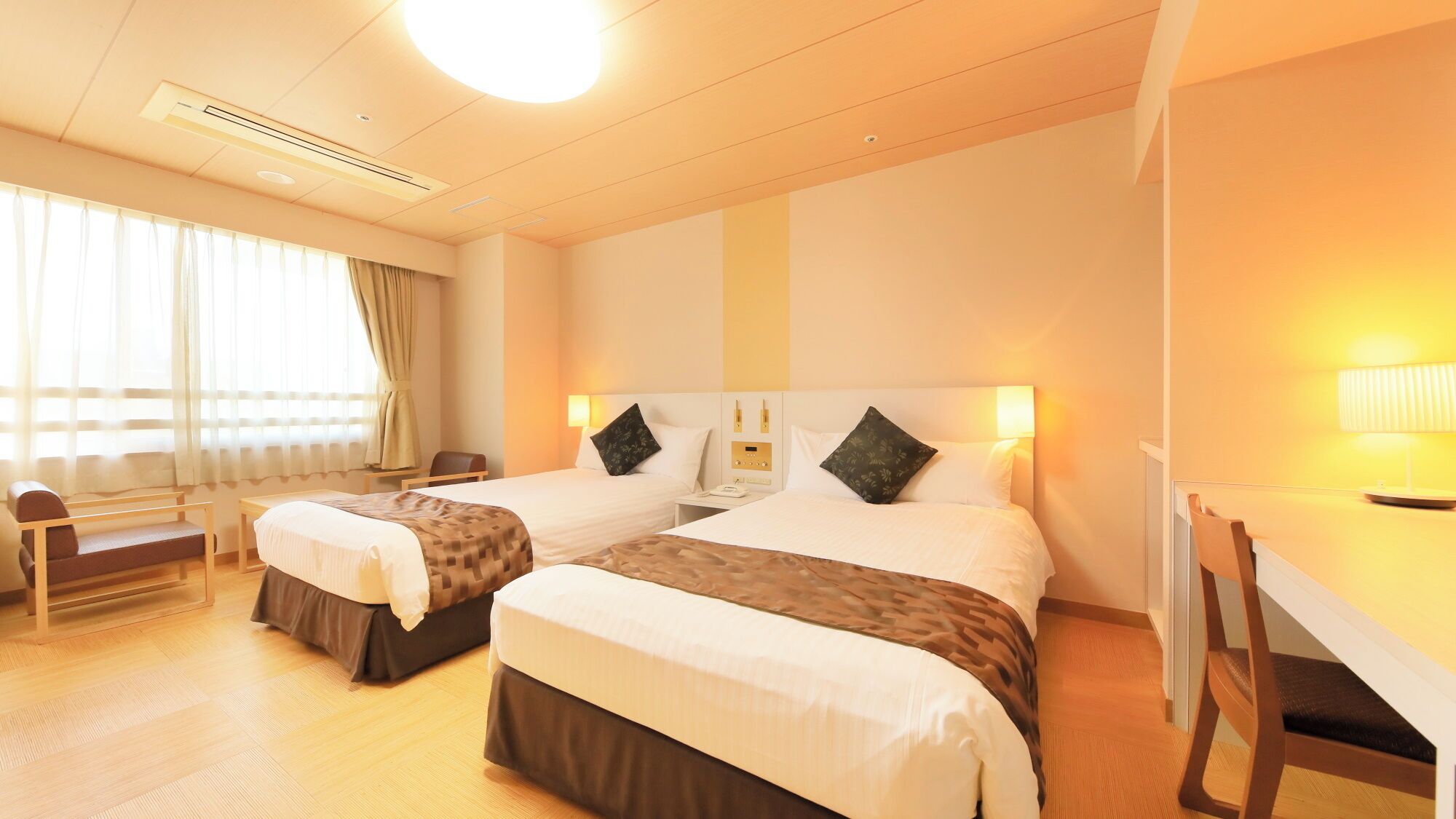 Habitación de hotel con dos camas, un escritorio, una silla y una ventana con cortinas.