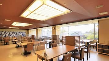 A spacious indoor dining area with multiple tables and chairs, large windows allowing natural light, and a ceiling with recessed lighting.