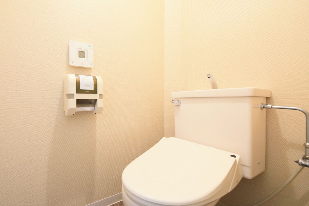 Un baño pequeño y sencillo con un inodoro, un dispensador de papel higiénico en la pared y una tubería visible.